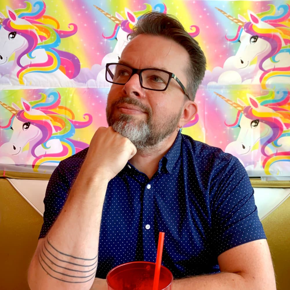 Photo of Boots, sitting in front of a backdrop of cartoon unicorns.